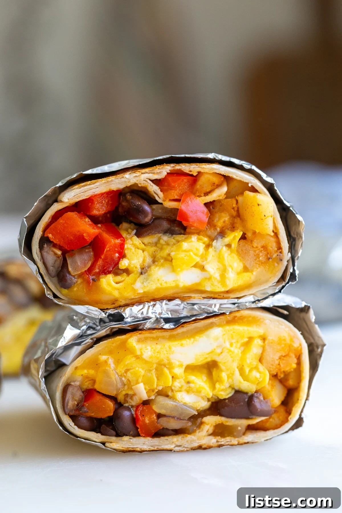A perfectly reheated meatless breakfast burrito, wrapped in foil for easy handling, cut cleanly in half to reveal its inviting interior filled with fluffy eggs, vibrant bell pepper, and wholesome black beans.