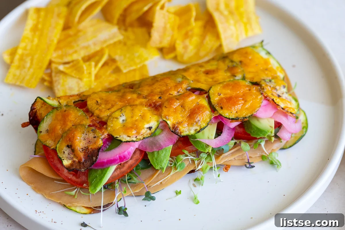 Skinny Zucchini Roll-Ups 3 Cheesy zucchini wrap stuffed with vegan meat, red onion, avocado, and tomato, served on a plate with chips for a complete meal.