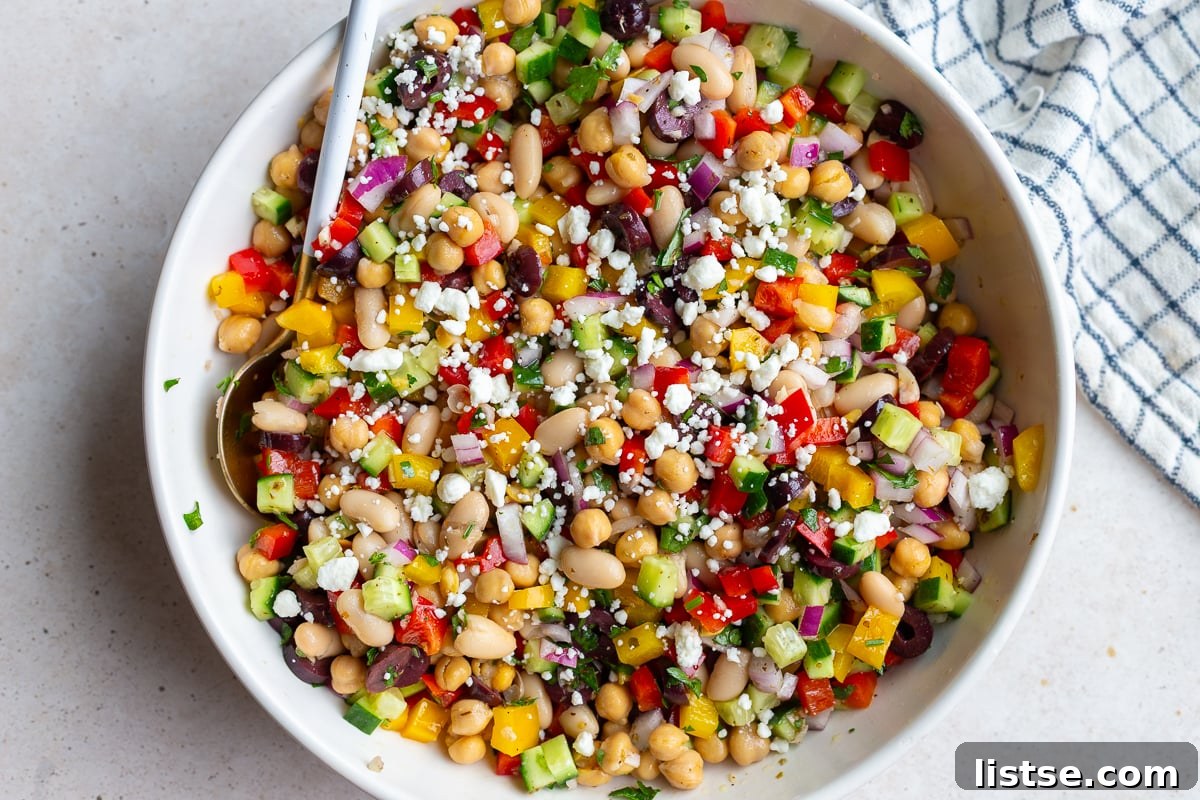 Vibrant Dense Bean Salad in a large serving bowl, featuring chickpeas, cannellini beans, colorful bell peppers, cucumber, red onion, olives, and feta cheese, all tossed in a zesty dressing.