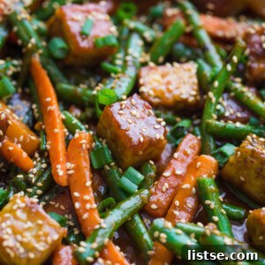 A vibrant and flavorful sesame ginger tempeh stir-fry, featuring crispy tempeh, colorful vegetables, and a glossy sauce, ready to be served over rice.