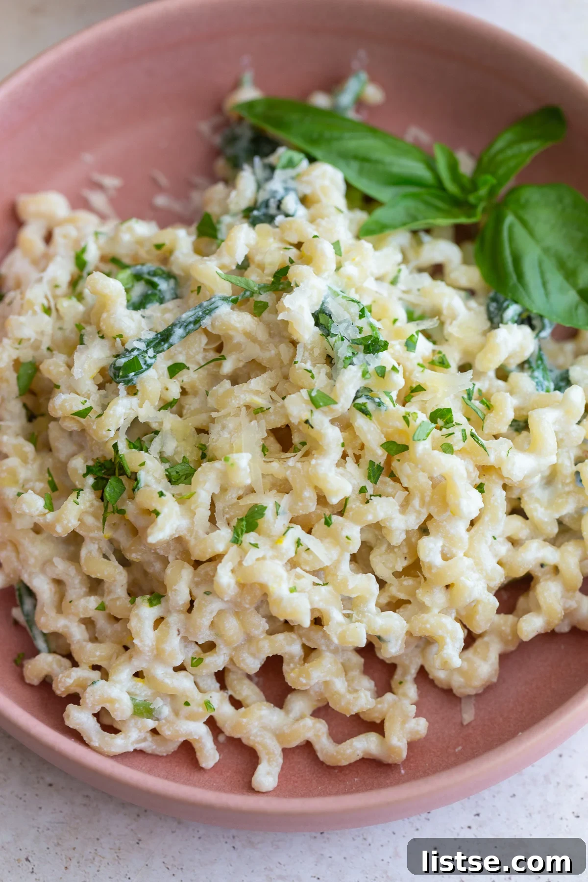 A large serving of creamy ricotta pasta garnished with fresh basil leaves and black pepper