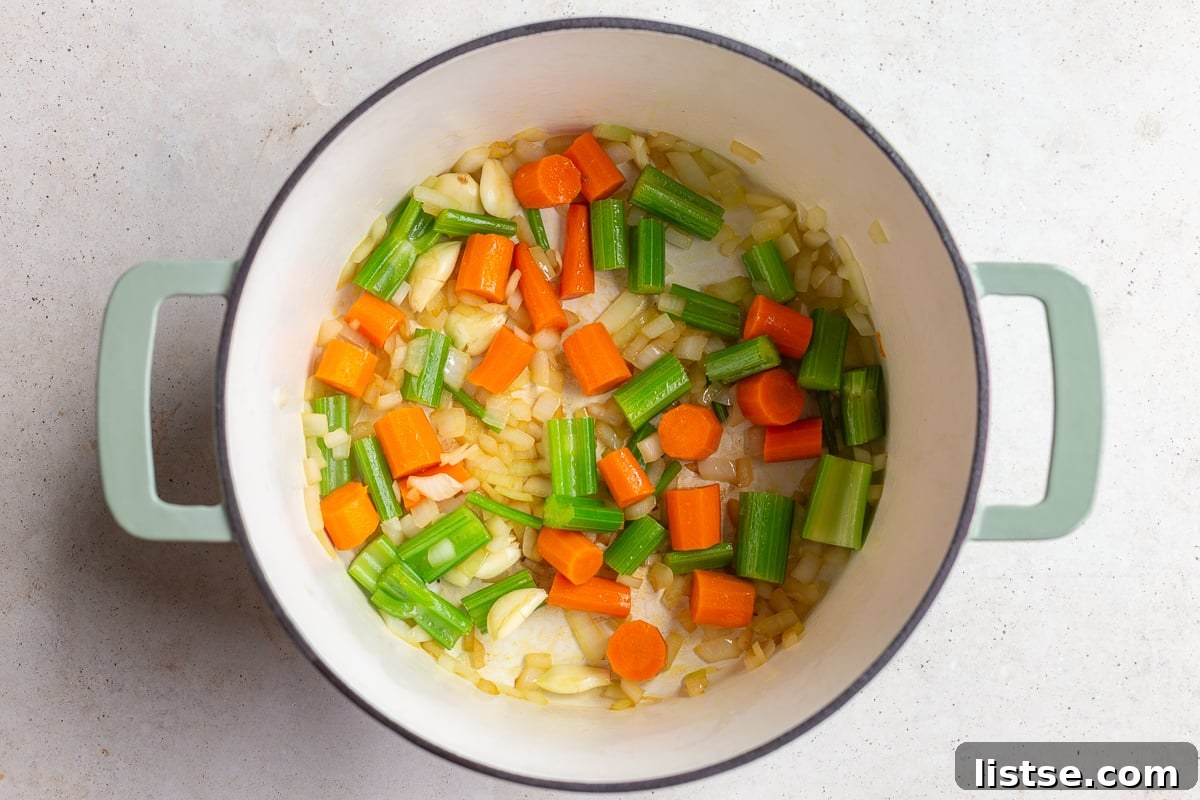 Diced carrots, celery, and onion gently sautéing in olive oil in a large pot, forming the aromatic base of the soup.