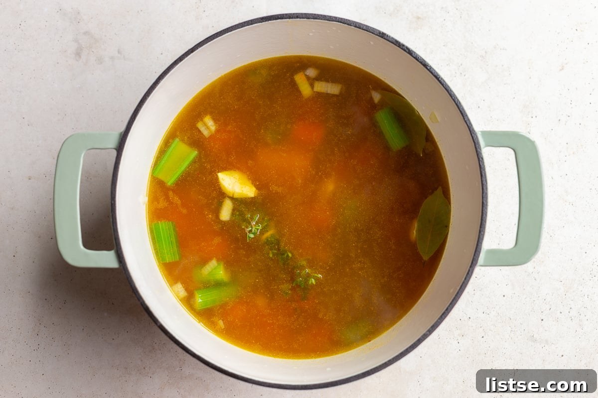 The soup base with sautéed vegetables, garlic, and vegetable broth, ready for simmering, with bay leaves and thyme visible.