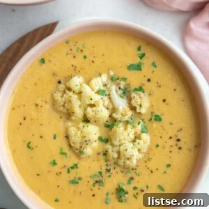 Big pink bowl filled with orange roasted cauliflower soup topped with roasted cauliflower florets and fresh herbs for garnish