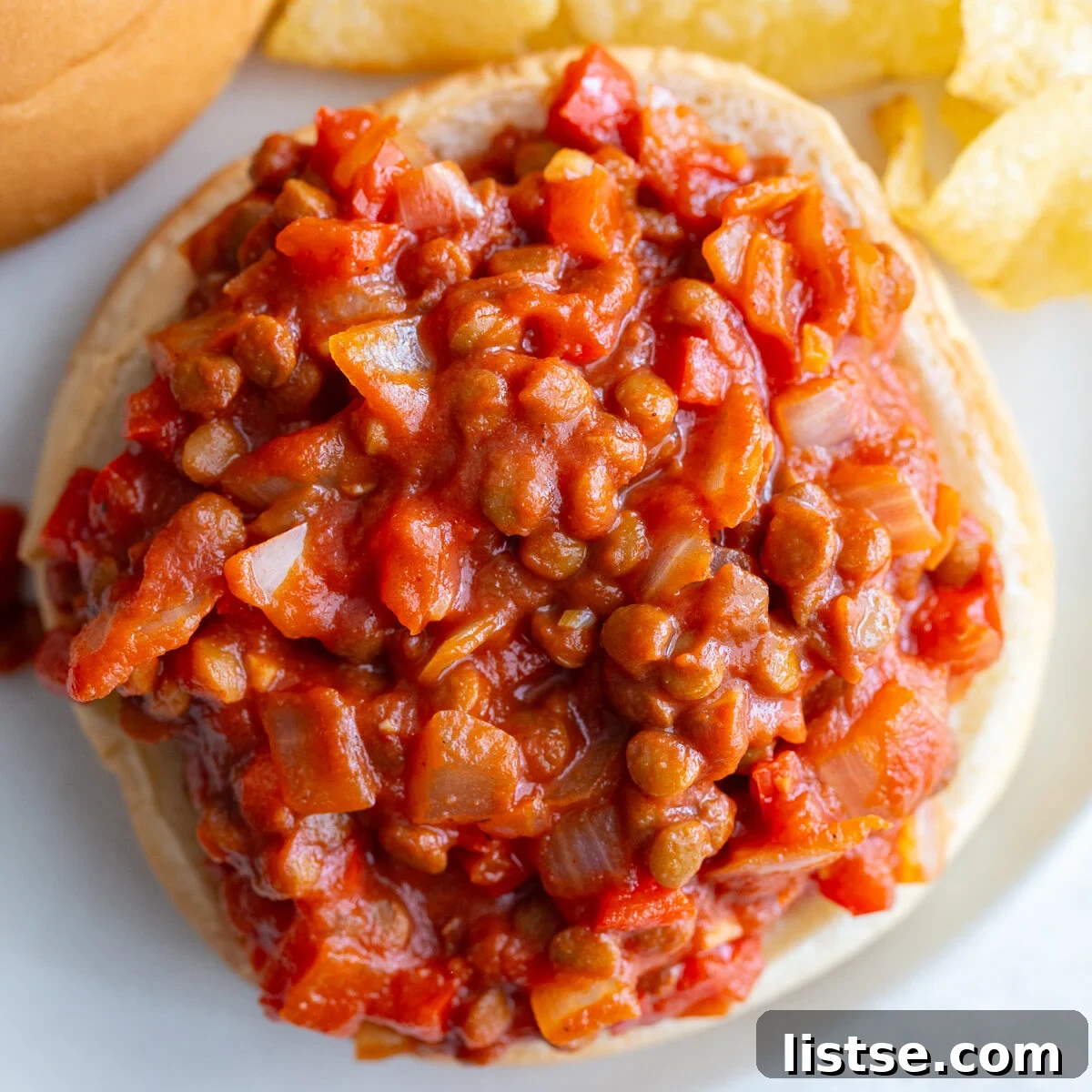 A close-up of a lentil sloppy joe on a toasted bun, with another one blurred in the background, ready to be devoured.
