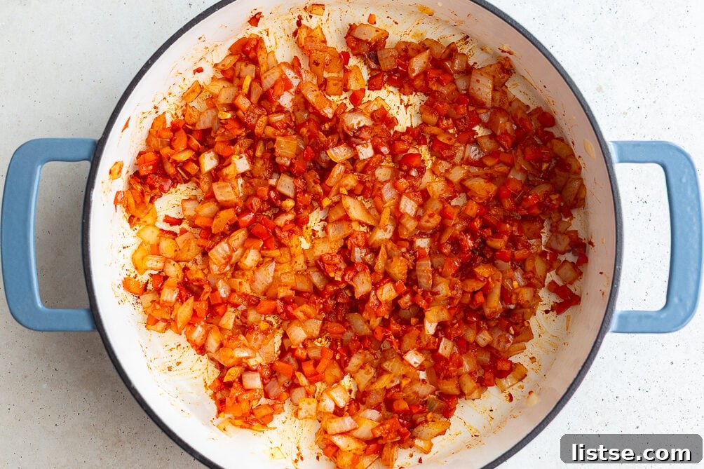 Step 2: Mixing tomato paste and spices into the sautéed vegetables in the pan.