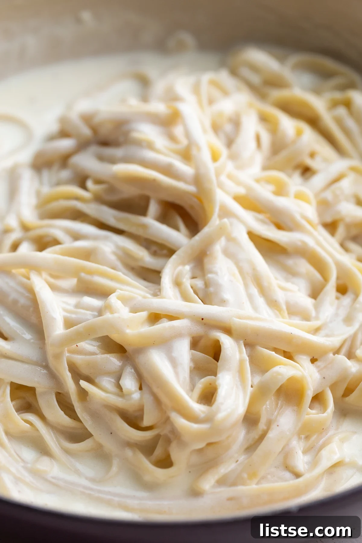 Luscious Homemade Alfredo in Minutes 5 A close-up shot of creamy Alfredo sauce coating fettuccine pasta in a bowl, ready to be served.