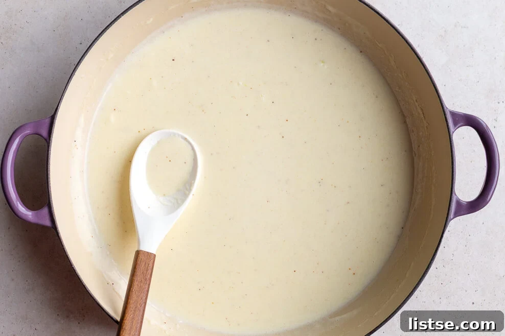 Luscious Homemade Alfredo in Minutes 7 Heavy cream being slowly whisked into a skillet with butter and garlic, a crucial step for making smooth, homemade alfredo sauce.