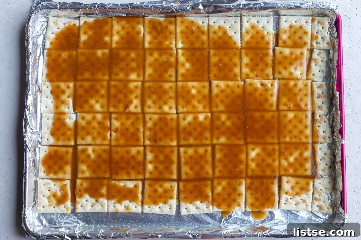 how to make christmas crack: picture showing the hot toffee poured on top of saltine crackers that are lined up on a baking tray