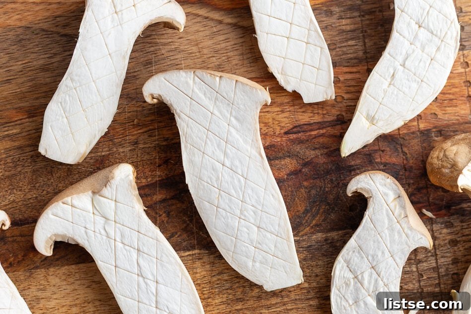 King oyster mushrooms scored on a cutting board, ready for cooking.