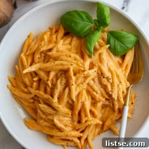 Spiral pasta coated in a rich roasted red pepper sauce, garnished with fresh basil in a wide bowl.