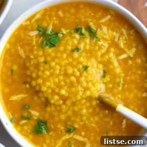 A comforting bowl of Italian Penicillin Pastina Soup with lemon slices and fresh herbs.