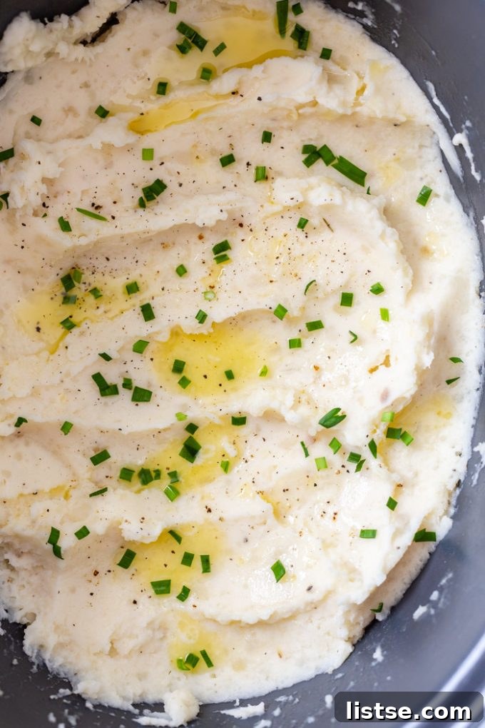 Velvety Slow Cooker Mashed Potatoes 5 Close-up of fluffy crock pot mashed potatoes in a slow cooker, garnished with melting butter and fresh parsley