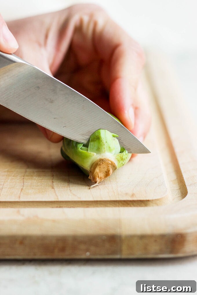 Quick and Crispy Sautéed Brussels Sprouts 4 A hand demonstrating how to properly cut off the tough stem end of a fresh Brussels sprout, preparing it for cooking.