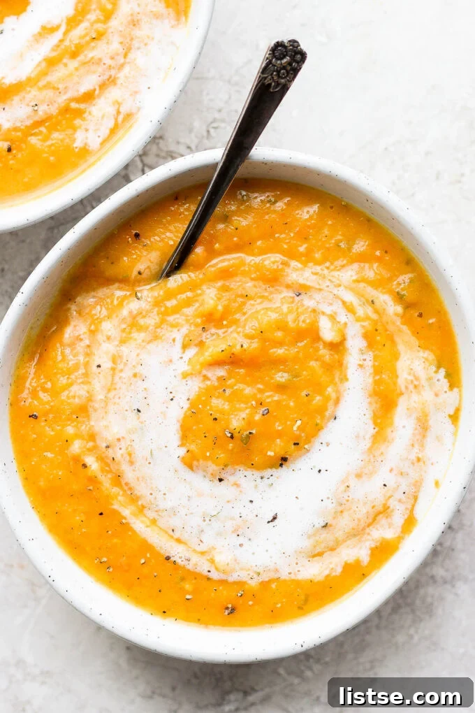 Creamy roasted acorn squash soup topped with an elegant swirl of plant-based cream, garnished with fresh herbs, in a white bowl.
