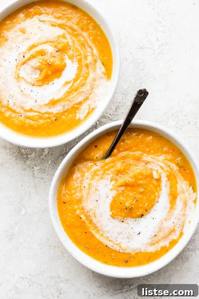 Two white bowls filled with golden, creamy acorn squash soup, garnished with a sprinkle of fresh parsley.