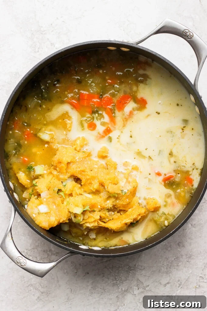 Adding tender, roasted acorn squash and plant-based milk to a simmering soup pot.