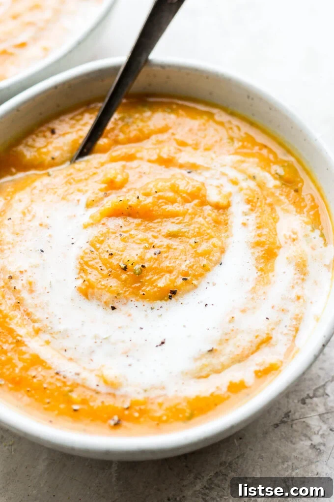 A close-up of a white bowl filled with creamy acorn squash soup, with a spoon resting in it, ready to be enjoyed.