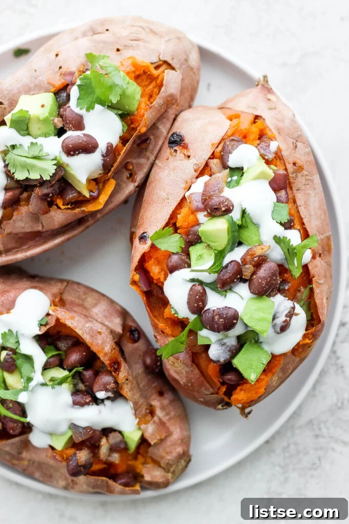 Sweet potatoes generously stuffed with a savory black bean mixture, topped with creamy avocado slices and a drizzle of vegan crema.