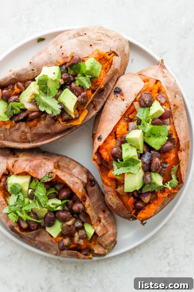 A vibrant close-up of a baked sweet potato, cut open and generously filled with a seasoned black bean mixture and creamy avocado chunks.