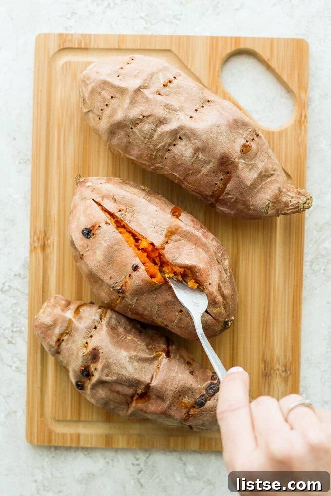 Two perfectly cooked, tender sweet potatoes resting on a rustic wooden cutting board, ready for stuffing.