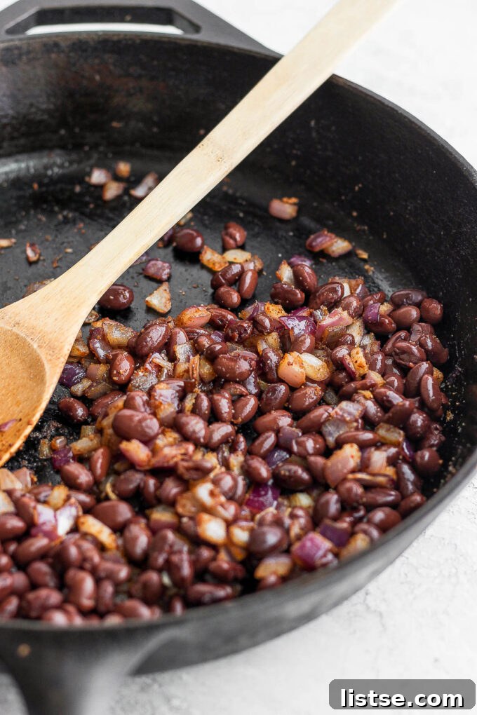 A close-up shot of seasoned black beans and finely diced onions sizzling in a skillet, filling the air with enticing aromas.