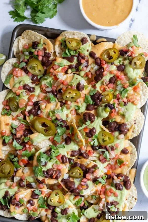A baking tray laden with vegan nachos generously topped with homemade cheese sauce and fresh toppings.