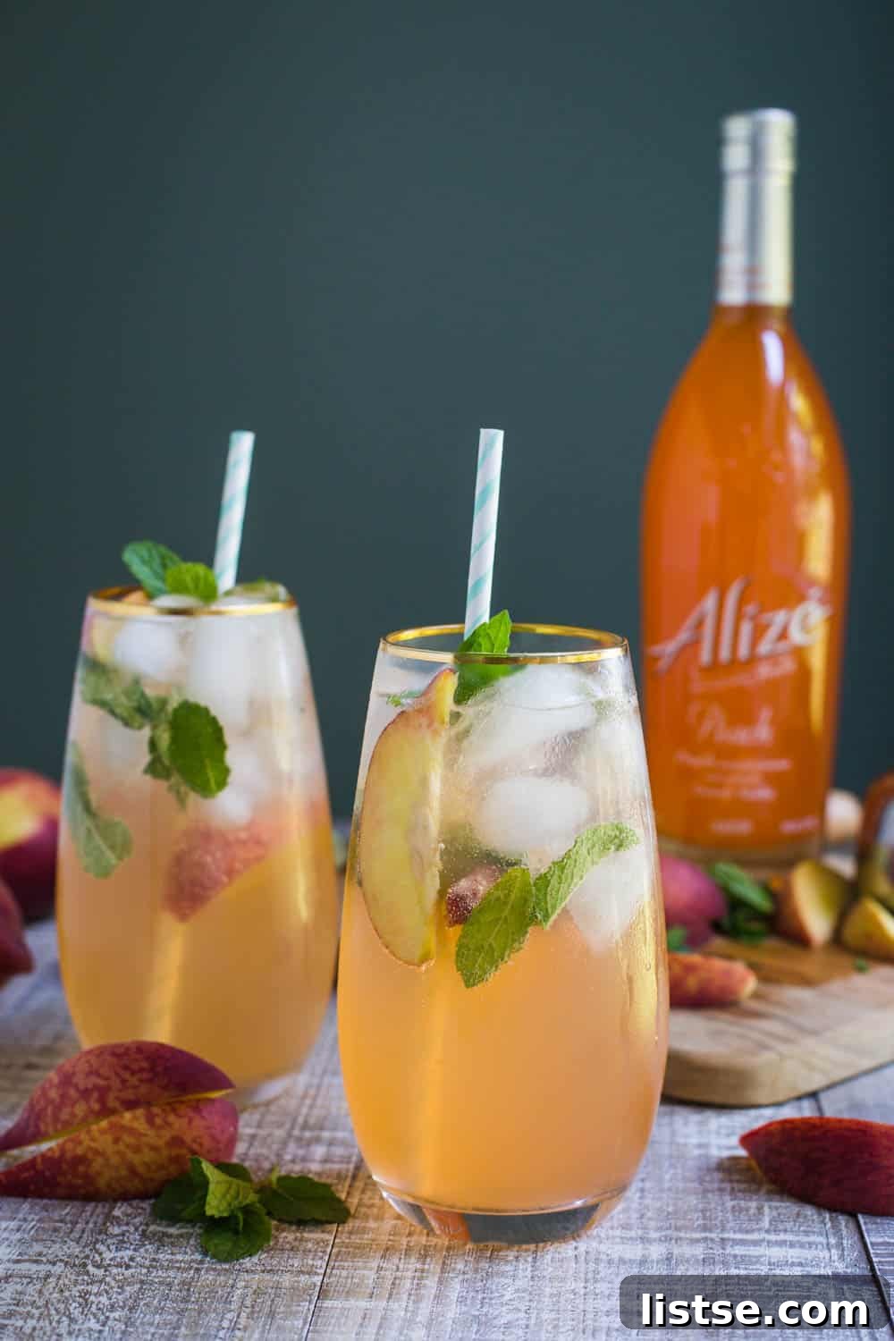 Two glasses of Peach Mojito garnished with peach slices and mint leaves, ready to be served.