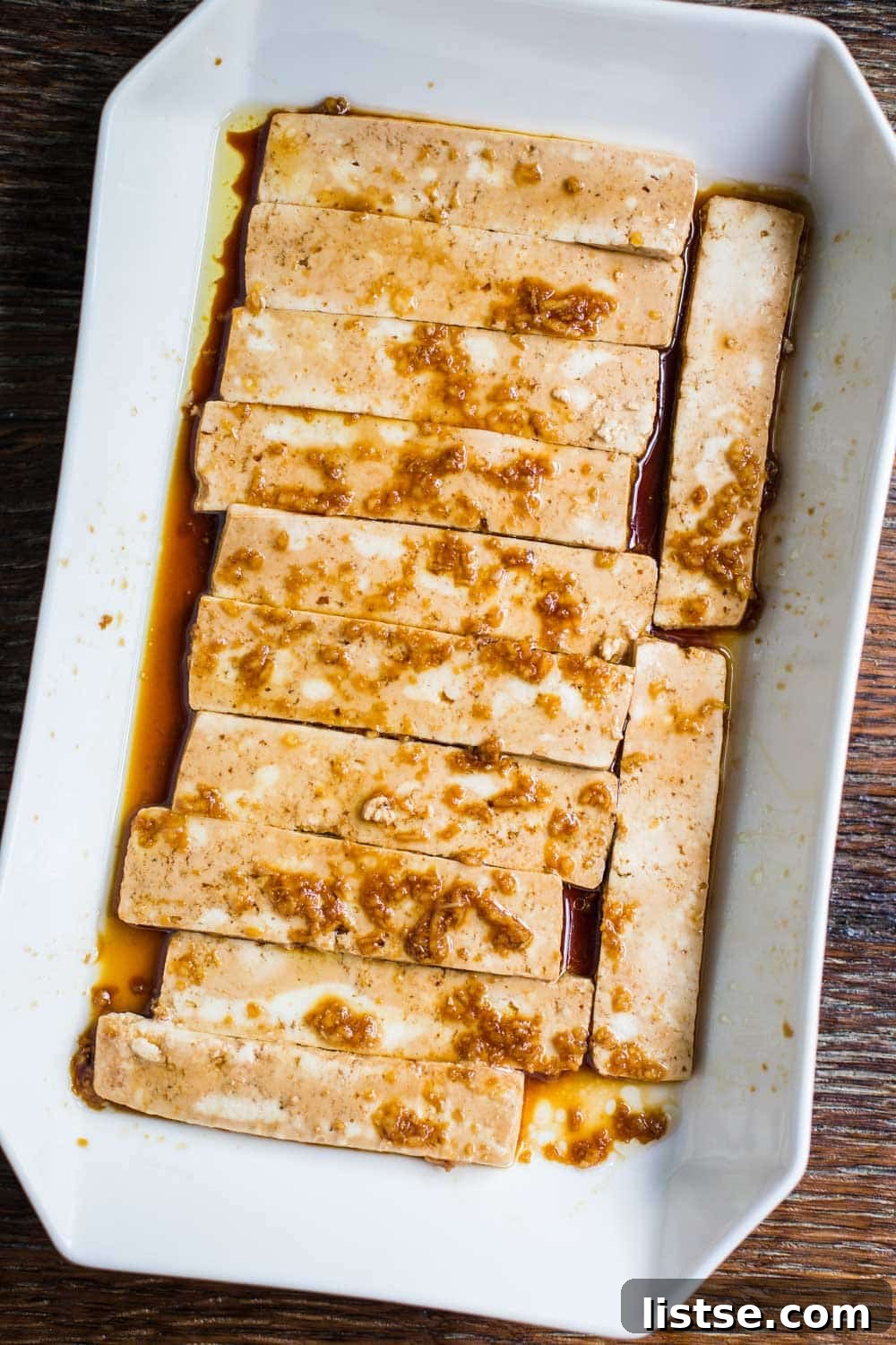 Slices of extra-firm tofu marinating in a shallow dish, absorbing savory flavors.