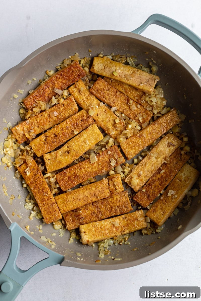 Marinated tofu slices being cooked to a golden brown in a large nonstick skillet.