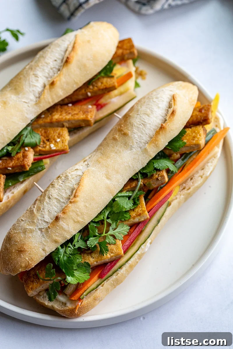 A close-up view of a Tofu Banh Mi Sandwich filled with vibrant ingredients, resting on a rustic French bread.