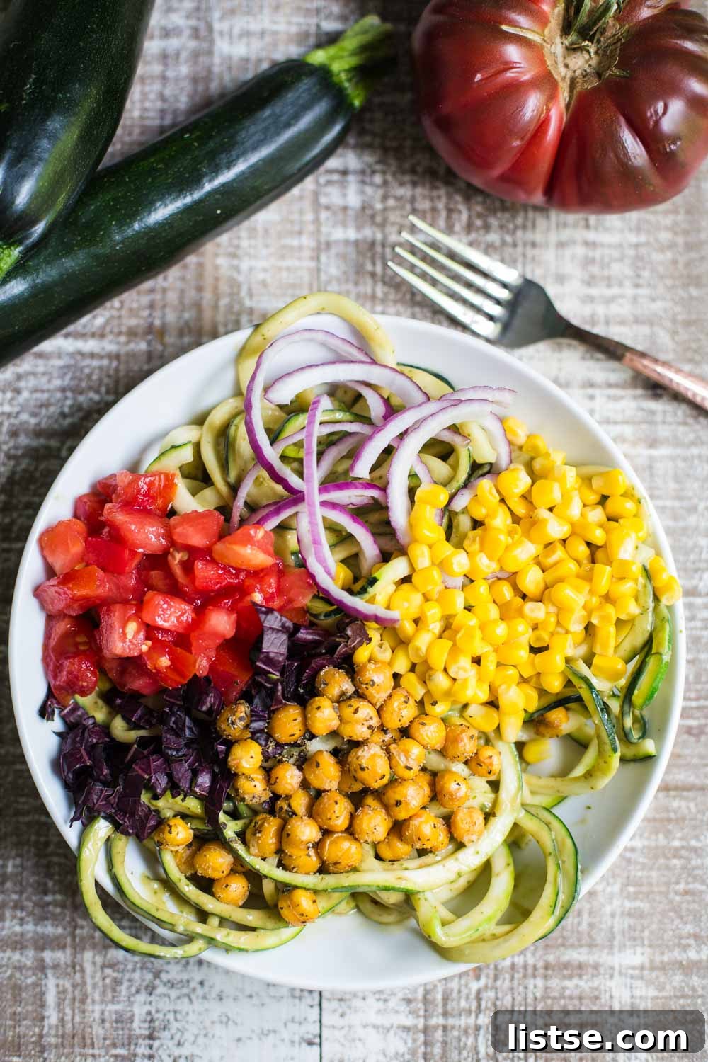 A vibrant bowl of Summer Harvest Zoodles, topped with roasted chickpeas, fresh corn, heirloom tomatoes, and purple basil