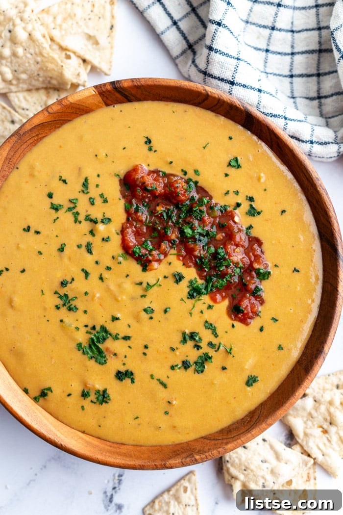 large wooden bowl filled with vegan salsa con queso and topped with salsa and cilantro. Chips on the side