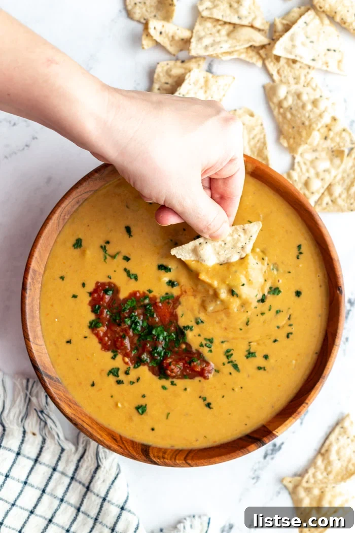 large wooden bowl filled with vegan salsa con queso and topped with salsa and cilantro. Chips on the side