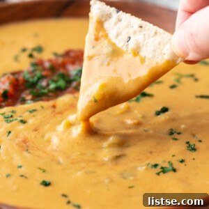 large wooden bowl filled with vegan salsa con queso and topped with salsa and cilantro. a chip scooping out some of the queso