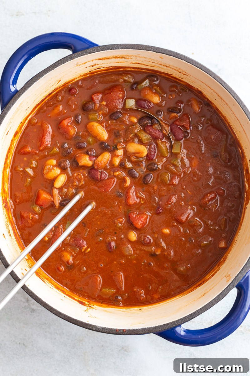 Ultimate Plant-Based Chili 8 A close-up shot of hearty beans, diced tomatoes, and savory broth being stirred together in a large, bubbling pot of vegetarian chili.