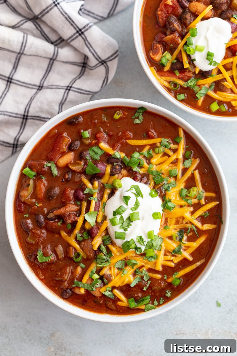 Ultimate Plant-Based Chili 10 A vibrant bowl of vegan chili, richly garnished with plant-based sour cream, shredded dairy-free cheese, and fresh green onions, ready to be enjoyed.