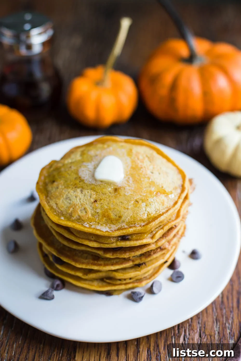 Close-up of fluffy Pumpkin Spice Chocolate Chip Vegan Pancakes drizzled with maple syrup and sprinkled with chocolate chips.