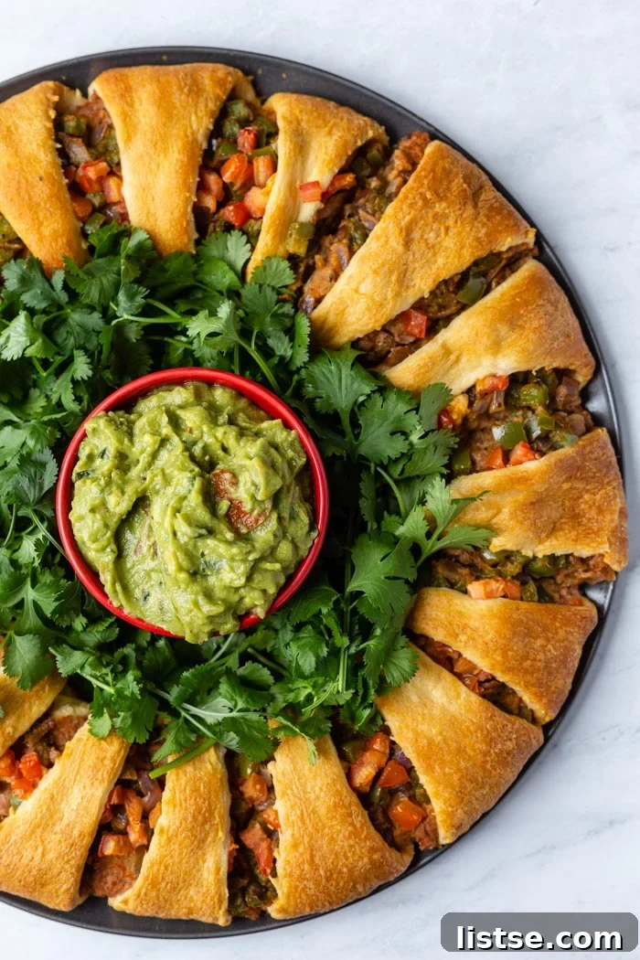 Plant-Powered Holiday Taco Wreath 2 Festive taco ring made from golden crescent rolls, generously filled with seasoned refried beans and colorful vegetables, with a vibrant bowl of creamy guacamole at its center. Perfect for a holiday party.