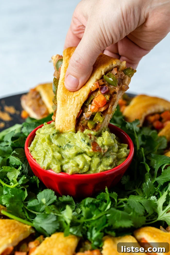 Plant-Powered Holiday Taco Wreath 3 Close-up view of a perfectly baked crescent roll segment from the taco ring, generously filled with refried beans and mixed vegetables, being dipped into a dollop of fresh, creamy guacamole. The rest of the golden, festive ring is visible in the background.