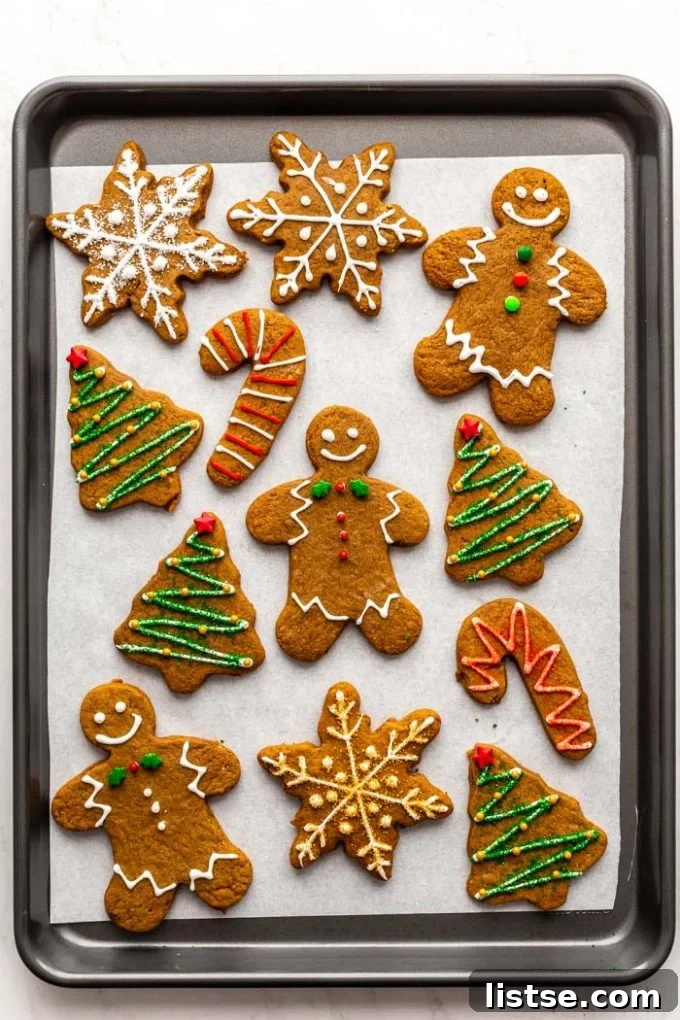 Plant-Based Gingerbread Delights 3 A festive array of vegan gingerbread cookies, beautifully decorated with intricate white icing patterns and colorful sprinkles, neatly arranged on a baking sheet, ready for holiday enjoyment.