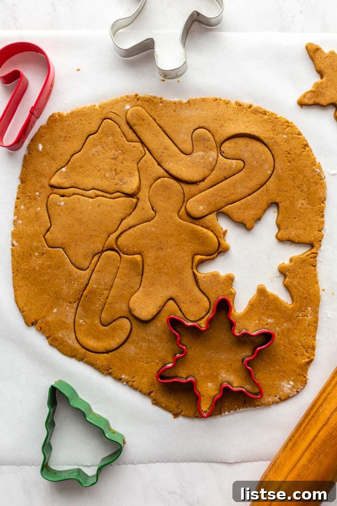 Plant-Based Gingerbread Delights 4 Close-up shot of hands using a gingerbread man cookie cutter to cut shapes from freshly rolled vegan gingerbread cookie dough on a floured surface.