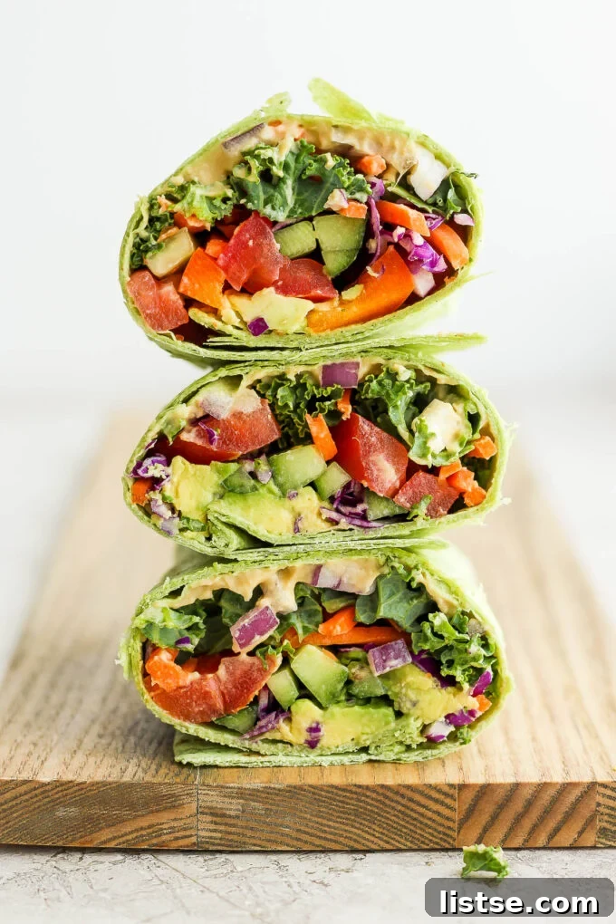 Three colorful veggie wraps stacked, revealing layers of vibrant vegetables and creamy hummus inside, showcasing a healthy and appealing meal.