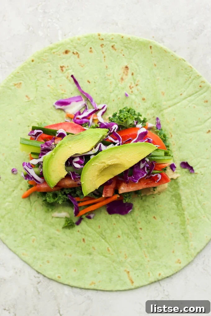 A vibrant spinach tortilla laid open with a generous spread of hummus and a colorful assortment of fresh, chopped vegetables ready for folding.