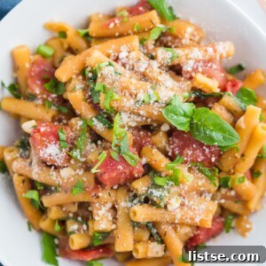 A white bowl brimming with red lentil pasta, cooked with tender tomatoes and garnished with fresh basil.