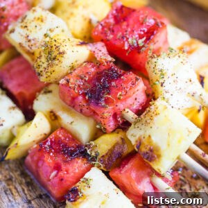 Appetizing close-up of grilled pineapple, mango, and watermelon cubes on a skewer.