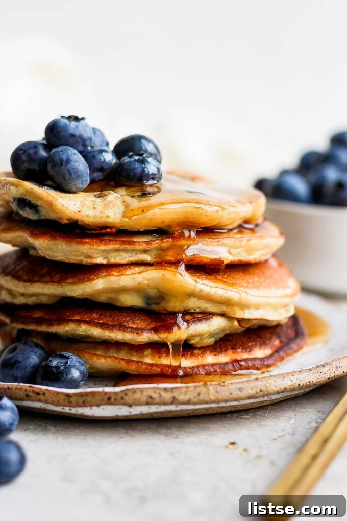 Power-Packed Banana Protein Pancakes 6 A stack of perfectly cooked banana protein pancakes on a white plate, garnished with fresh blueberries and a light drizzle of syrup.