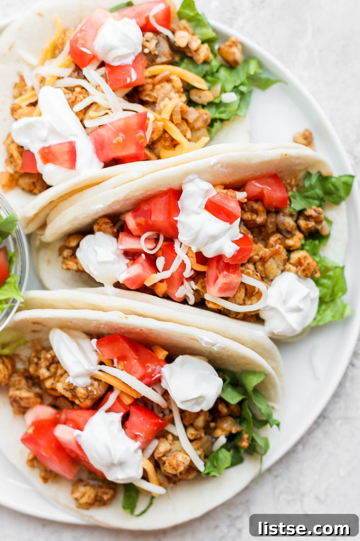Fully assembled tempeh tacos on flour tortillas, topped with melted cheese, fresh tomatoes, and cilantro