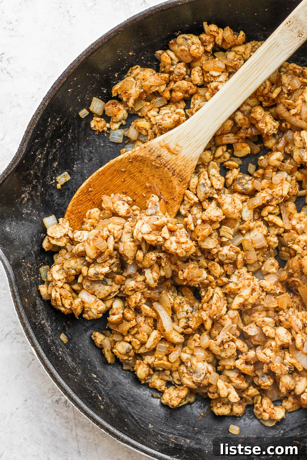 Crumbled tempeh taco 'meat' cooking in a pink skillet, seasoned with spices