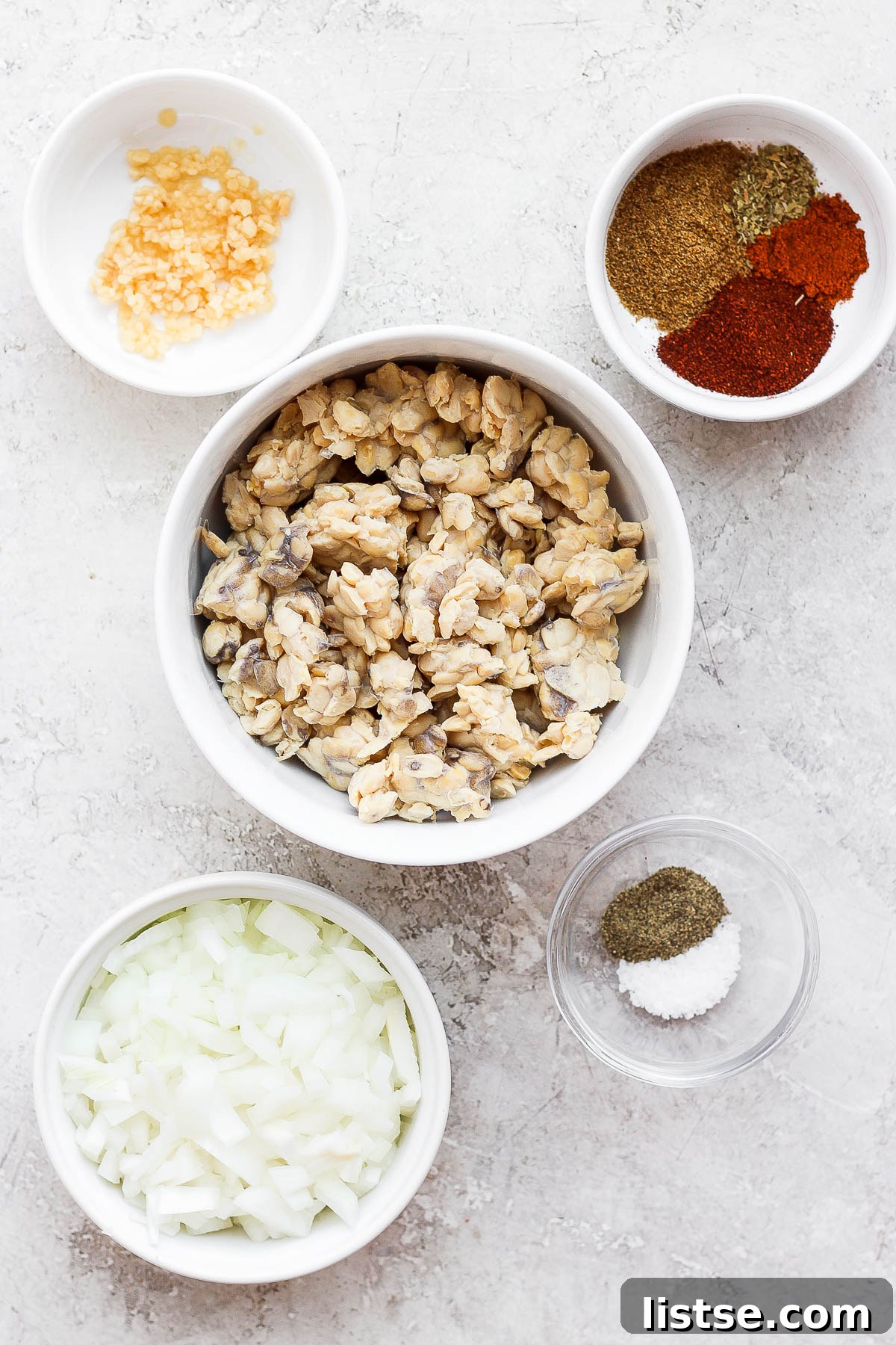 All the fresh ingredients laid out for making tempeh tacos, including tempeh, spices, onion, and garlic